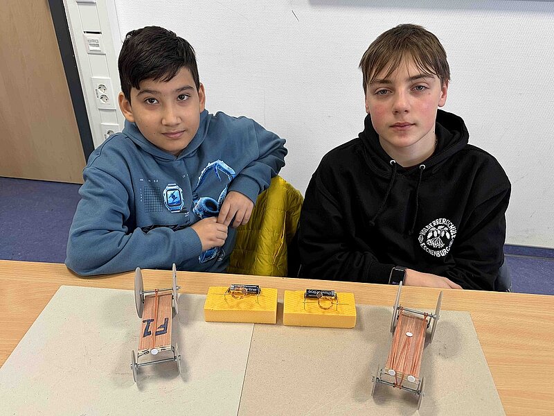 Rahman Niazi und Philip Luginbühl (7G2) mit ihren fertigen Rennwagen und einem funktionierenden Modell eines Elektromotors.
